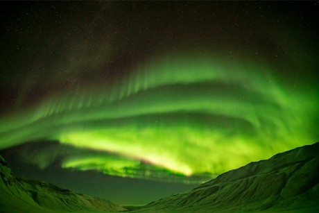 A view of the northern lights through a snow-covered mountain valley.
